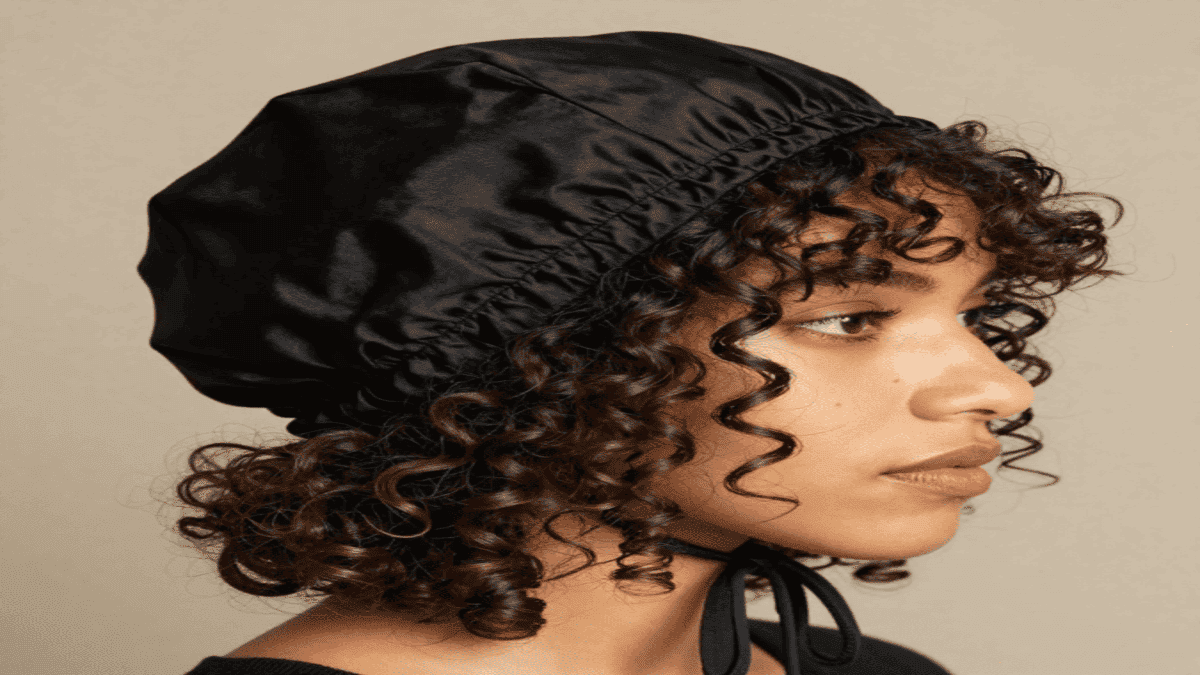 Woman with defined curly hair wearing a mulberry silk bonnet at night, showing how Silk Bonnets for Curly Hair help prevent frizz and breakage
