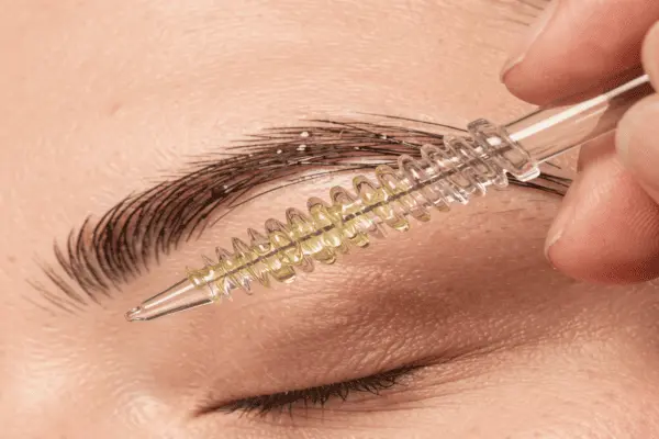 Close-up of a person using a clean mascara wand to apply oil to their eyebrow
