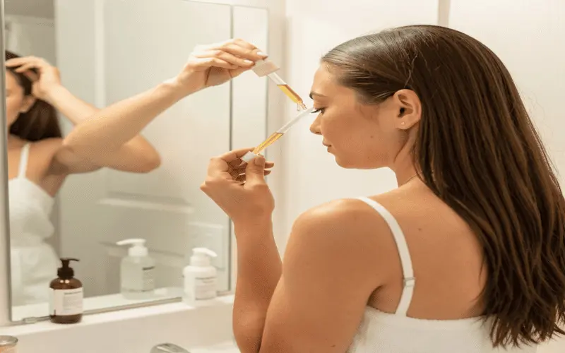 Scalp Serum Application Technique A woman applying hair growth serum directly to her scalp using a dropper.