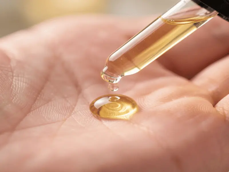 A glass dropper dispensing exactly three drops of clear Vitamin C serum into a palm.